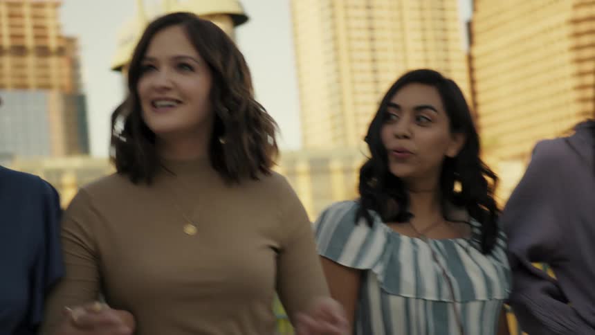 A group of female friends smile and laugh while walking together in a city