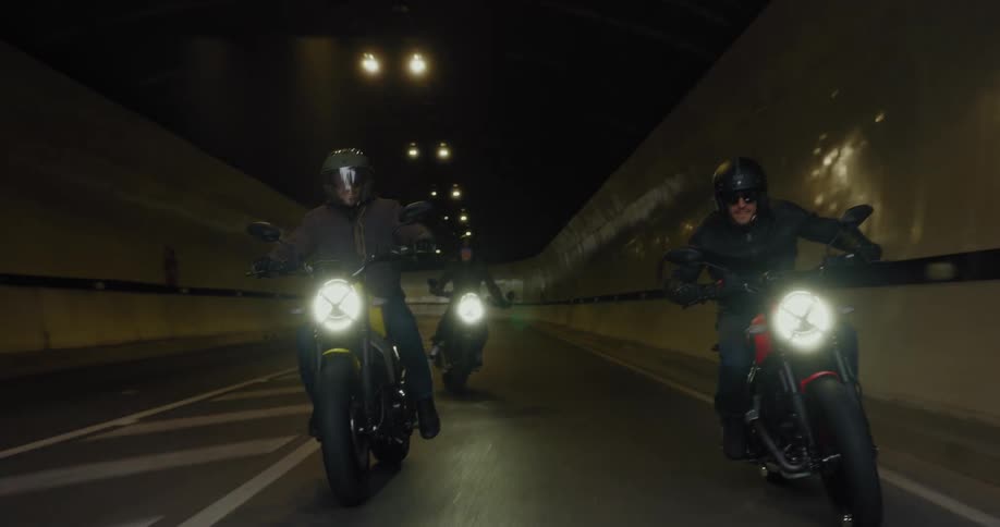 Three men emerge from the tunnel on motorcycles