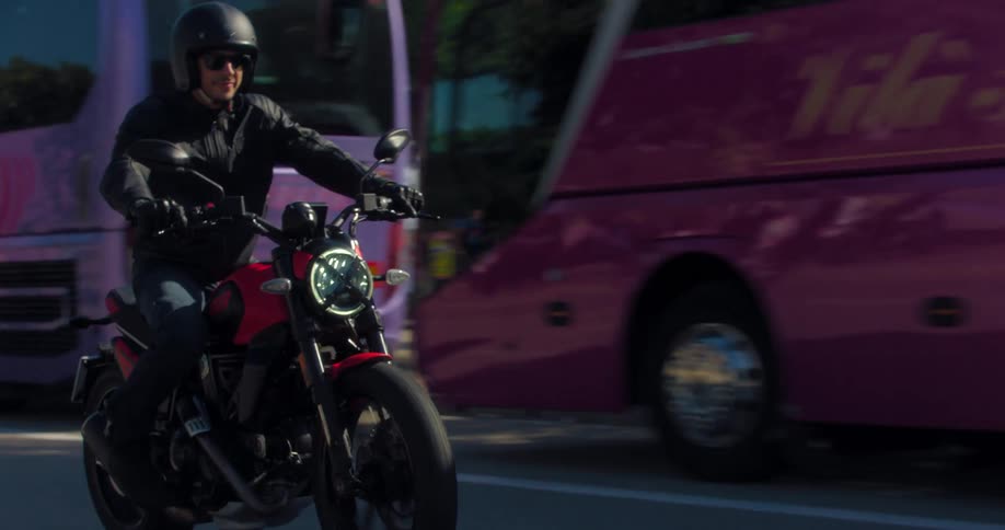 Motorcyclists on the road driving near buses and people walking on the sidewalk