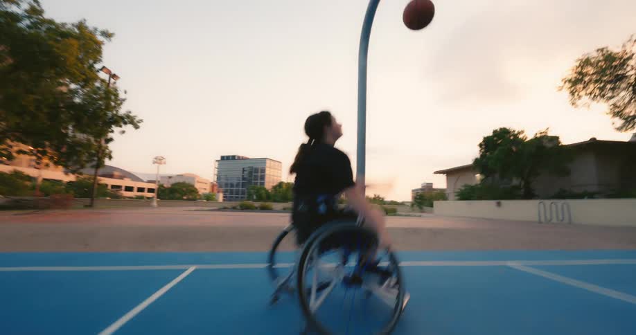 A female in a wheelchair shoots a basketball on a public court in a park