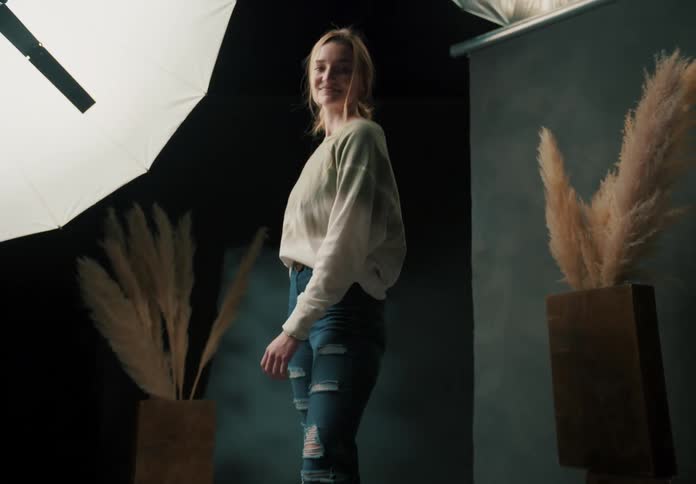 Female model walks over the camera track in a photography studio before turning to smile and pose