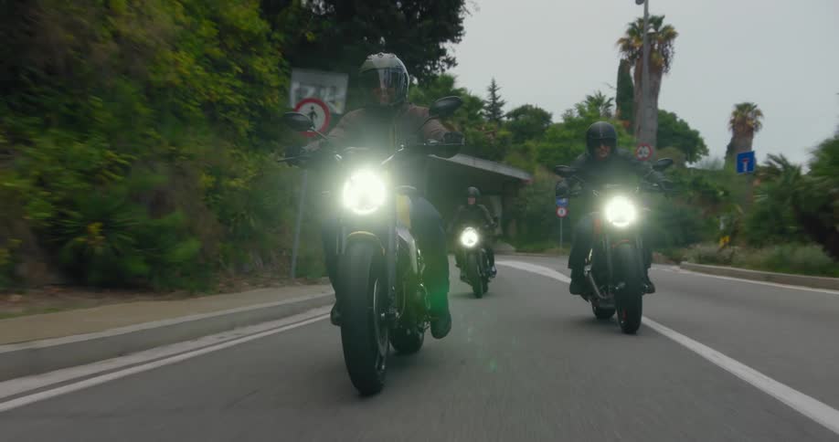 Three people ride motorcycles under a bridge and down a road