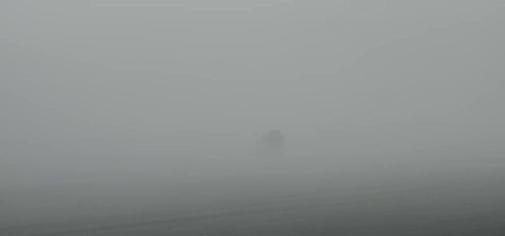 An suv drives across a sandy beach as mists blow over it