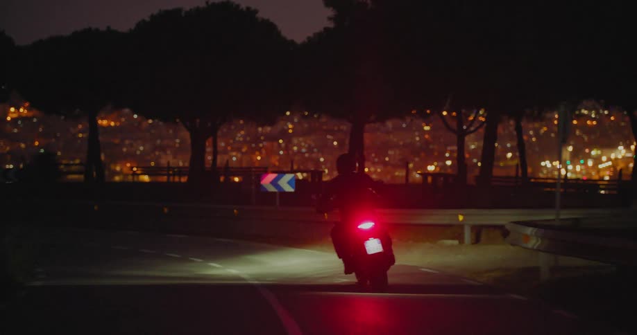 Motorcyclist rides along the highway on the outskirts of the city at night