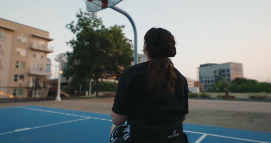 A woman moving around in a wheelchair on a basketball court while shooting the ball into the basket