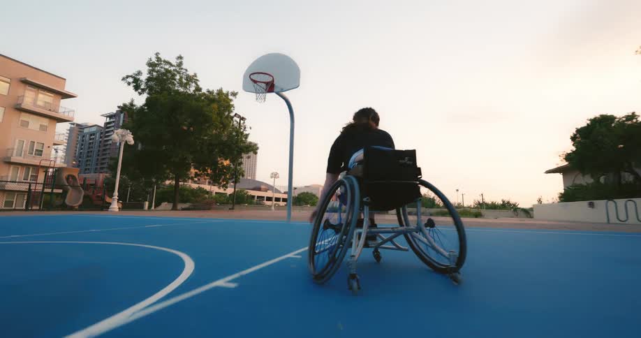 A woman in a wheelchair pushes herself across a basketball court to make a shot
