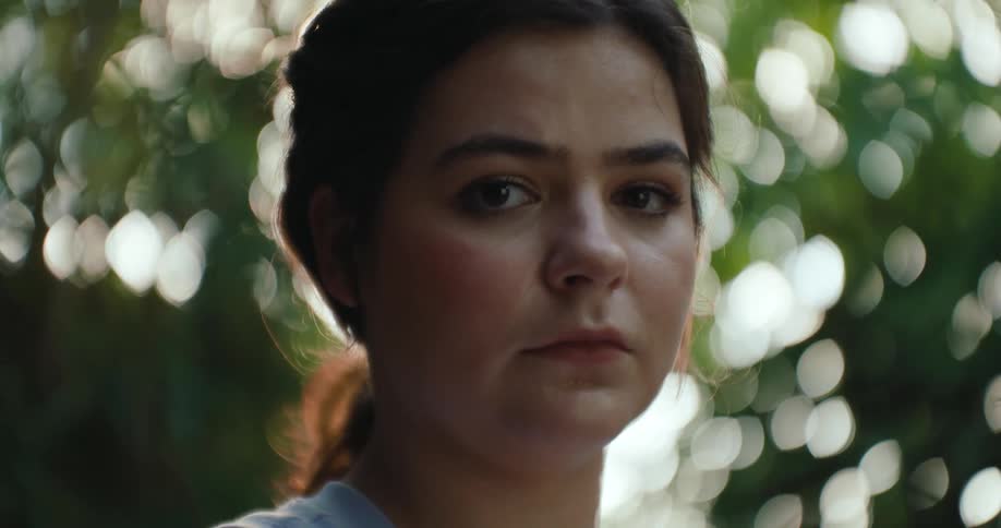 A teenage girl looks sad while standing outdoors by trees