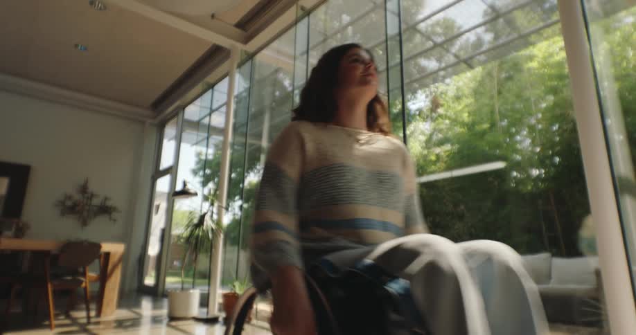 A woman in a wheelchair rolls herself through the living room of a house
