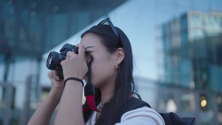 A woman is holding a camera up to their face with an urban background softly out of focus