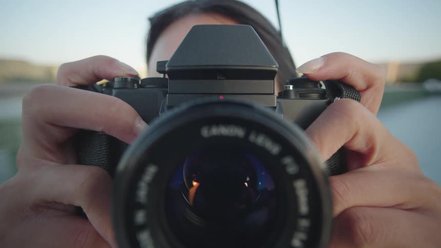A closeup of a persons hands pressing the shutter button on a vintage film camera with a large lens (POV)