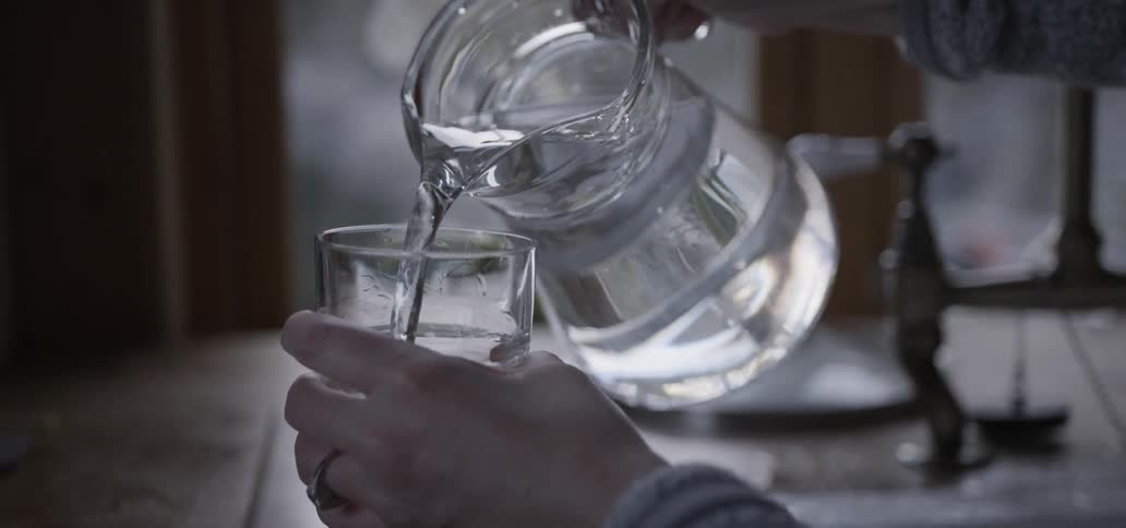 Woman pouring water into a clear glass from a clear-glass pitcher
