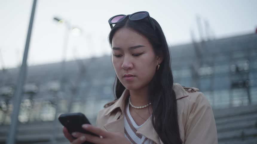 A young woman with sunglasses hanging from her hair is typing on a cell phone that is in her hands