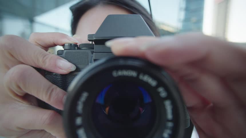 A closeup of a persons hands adjusting the focus on an analog camera lens (POV)