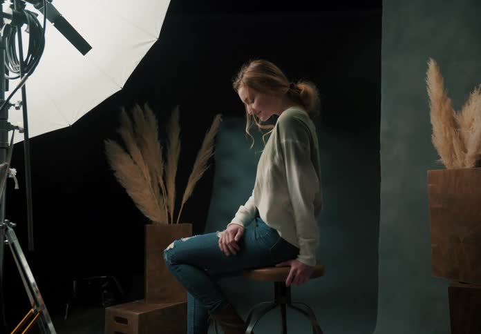 A photography studio setup with a young woman posing surrounded by professional lighting equipment and decorative elements