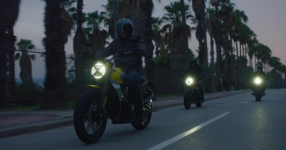 Motorcyclists ride motorcycles along a highway after dusk