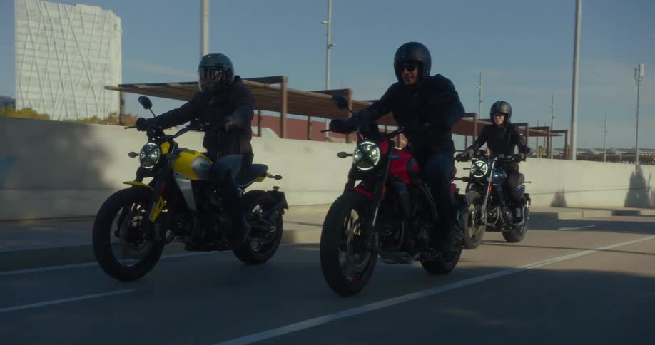 Three bikers with black leather jackets and colorful motorcycles riding on an asphalt street in a city at daytime