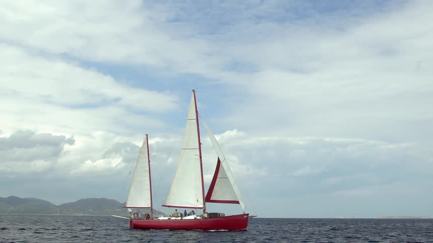 Friends ride in a sailboat with the foggy shore in the distant background on a cloudy day