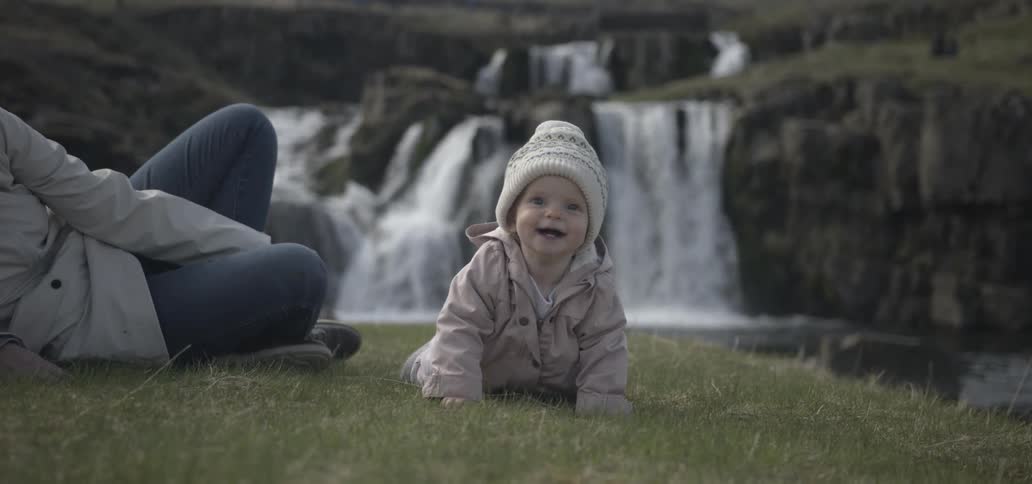 Baby and mother sitting at the edge of the water near a waterfall