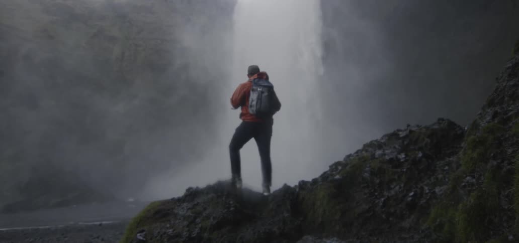 A man stands looking at a waterfall