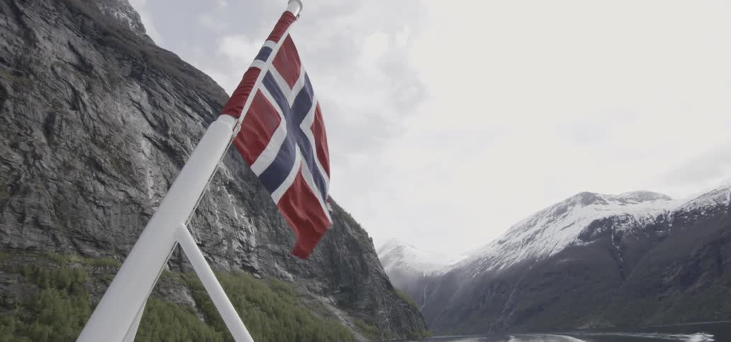 Flag flying from the rear of a boat moving down the river running between mountains