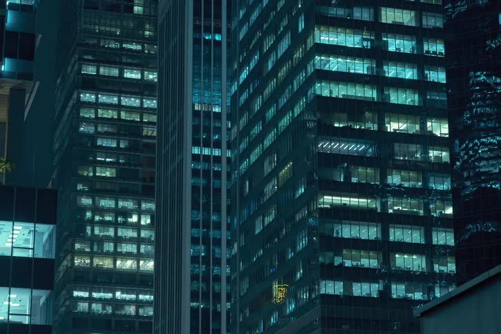 A time lapse of high rise office buildings in a city at night with lights in the windows on different levels turning on