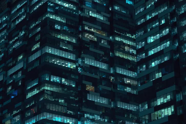 The lights in the apartments of a large building are turning on as dawn breaks
