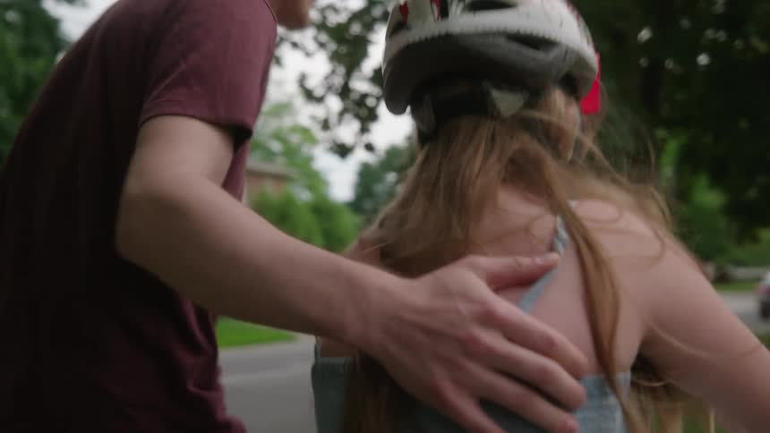 Close up of a fathers hand on his daughters back as he guides her while she rides a bike wearing a helmet