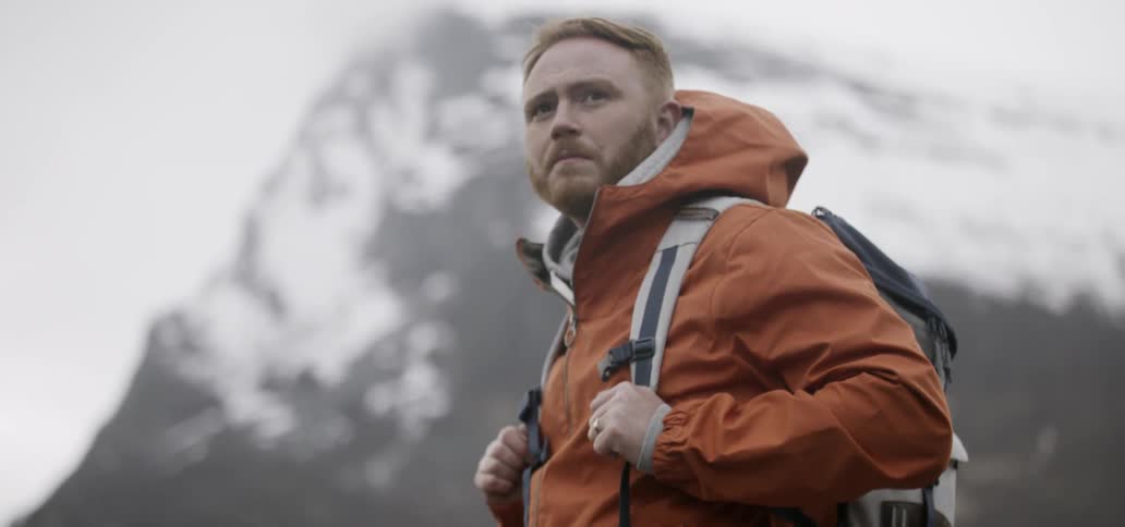 A man standing by a snow covered mountain on a cloudy day