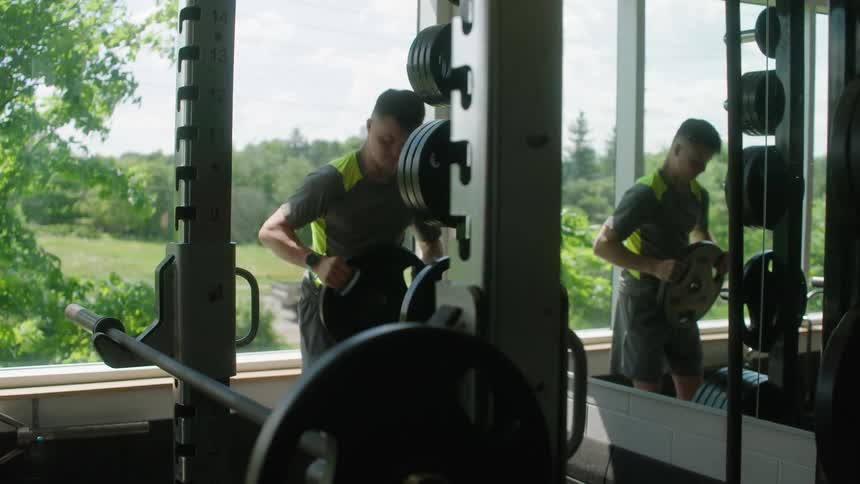 A man picking up a weight plate and placing it on a bench press bar