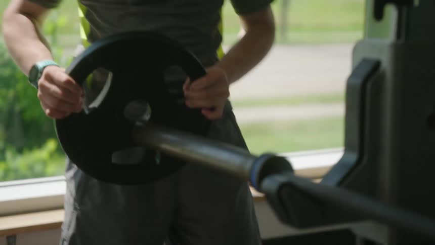 A young man with down syndrome adjusts weights on a barbell rack