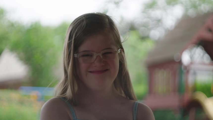 A little blonde girl with glasses is giving a smile while looking forward