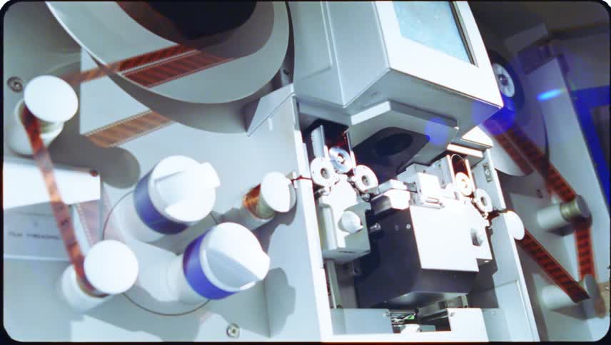 Close up of a large machine with flashing lights and film being fed into it