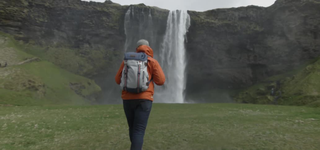 A person wearing a backpack walks toward a waterfall