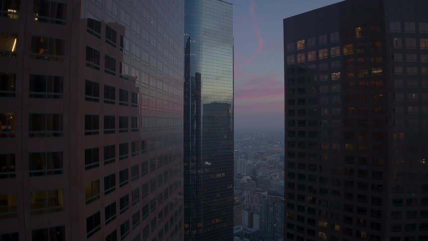 Rising upwards over high rise buildings in a city in blue hour before night