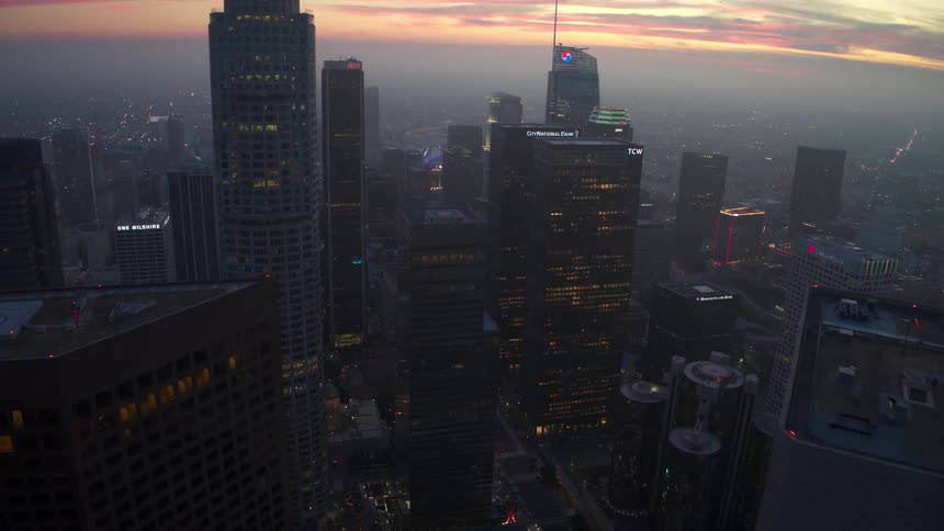 An epic aerial view of a city skyline during dusk twilight with several illuminated skyscrapers