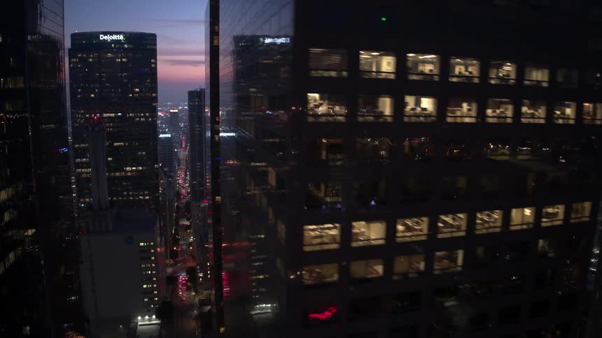 A sweeping aerial view of a city skyline during twilight with several illuminated reflective skyscrapers