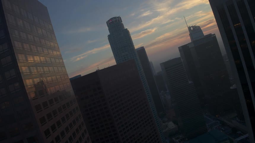 An sweeping aerial of high rise buildings in a city as the sun sets on the horizon