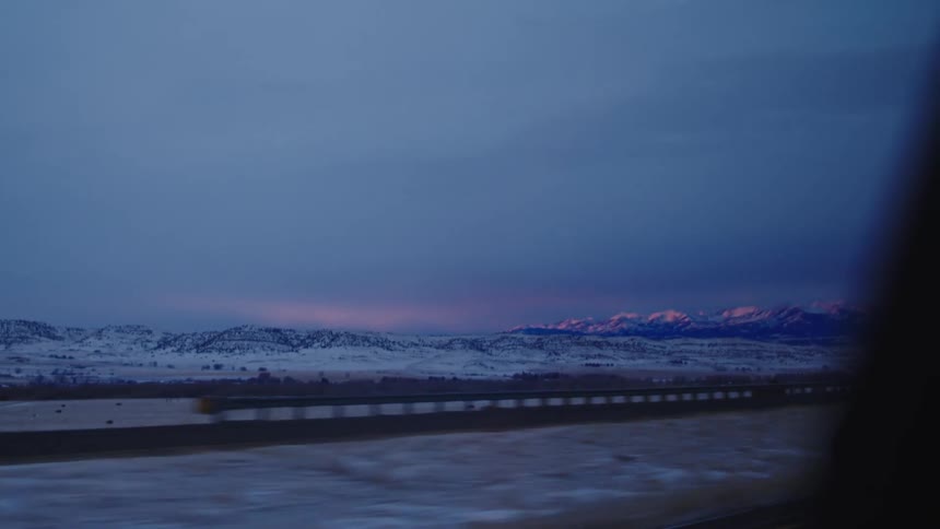 Twilight scene with snowcovered landscape and pinkish light on distant mountain peaks
