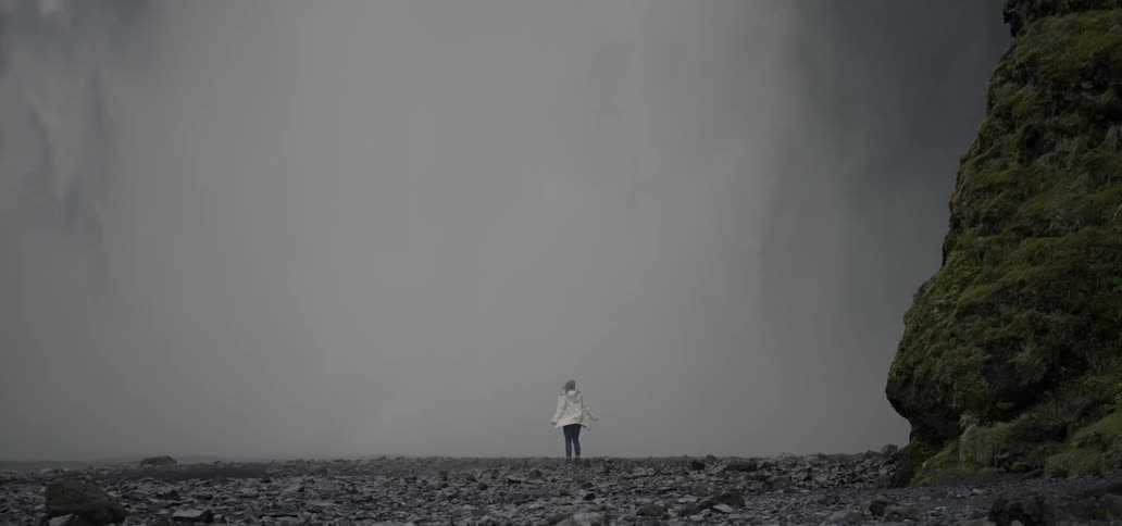 A woman standing at the foot of a large waterfall