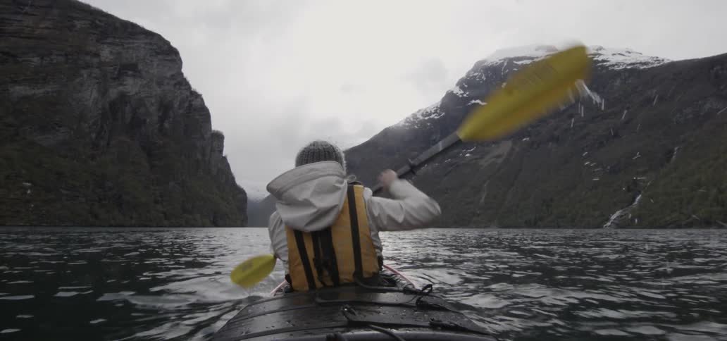Kayaker moving towards a  path between two mountains on a cloudy day