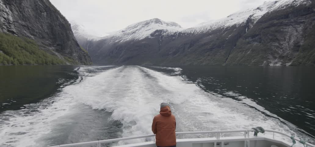 Person standing at the rear of a boat watching the waves formed from the moving craft