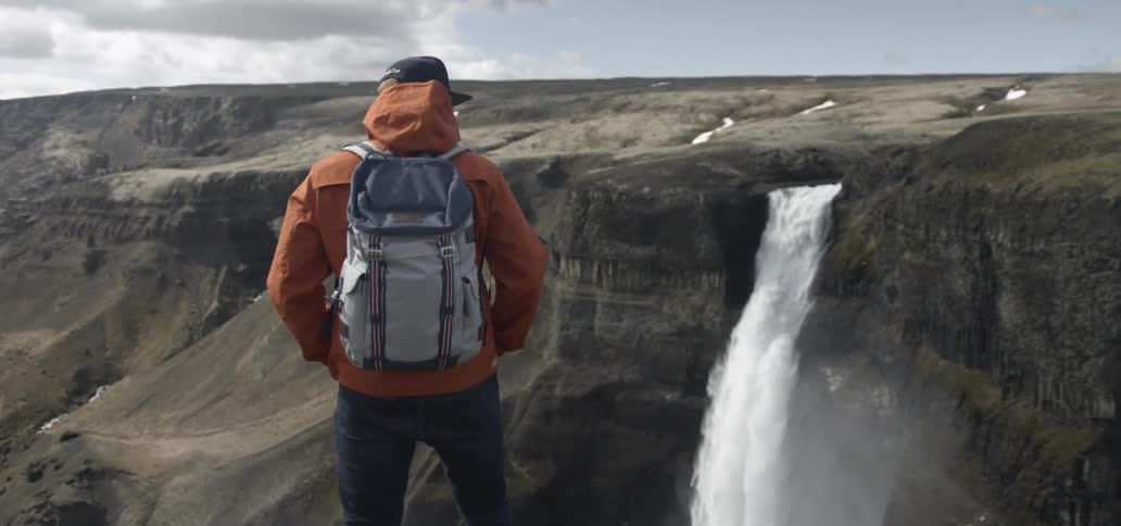 A hiker watches a waterfall cascading over a cliff