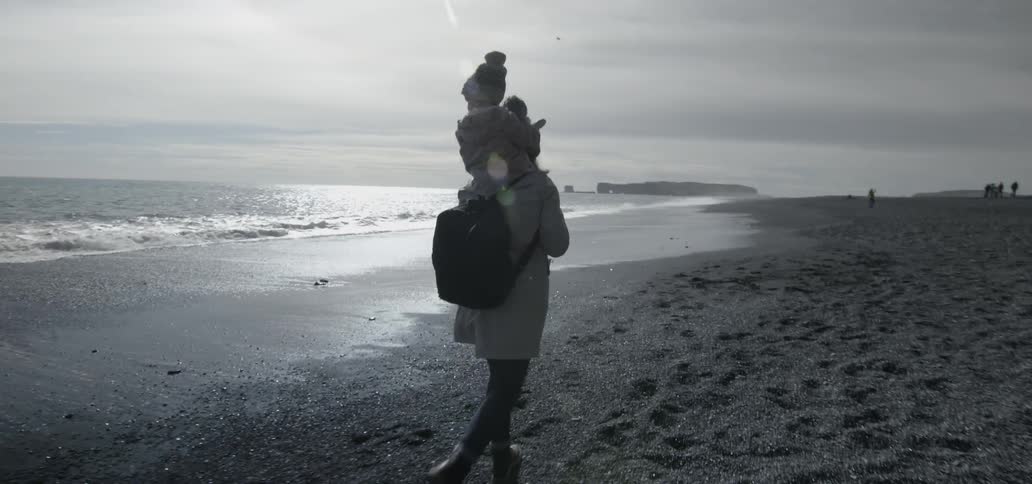 A man is walking along the beach carrying a child on his shoulders