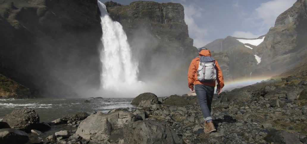 Hiker traversing a rocky area  with a waterfall in the background