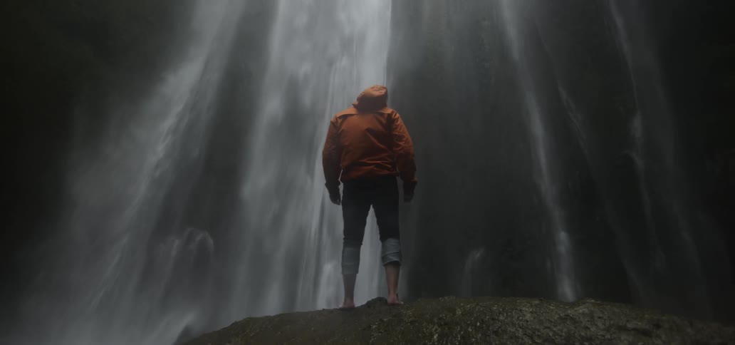 A man walking very close to a waterfall