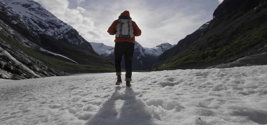 Hiker walking a snowy valley headed towards a cloudy sunset