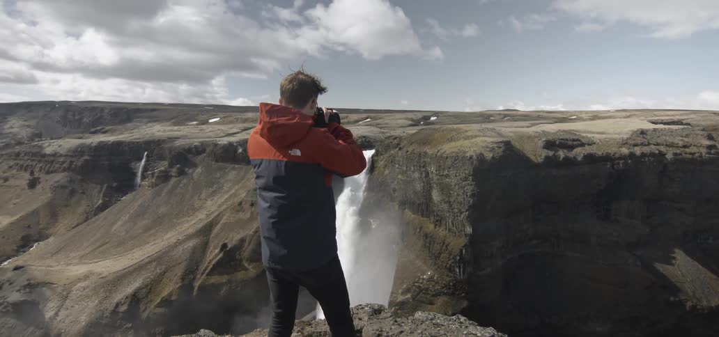 A man photographs a waterfall from atop a cliff