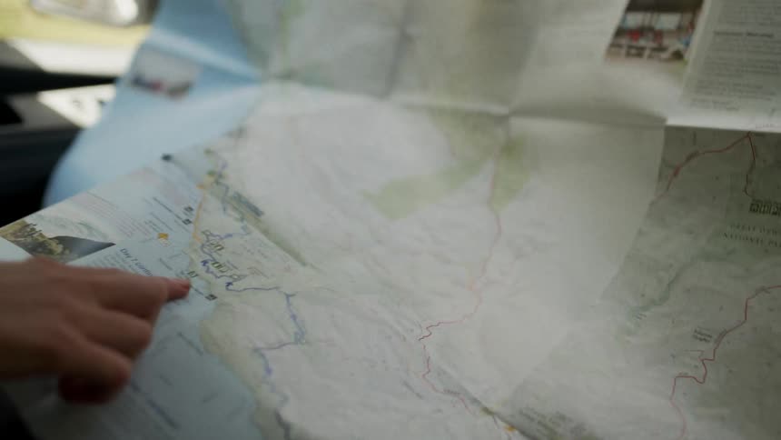Passenger navigates using a unfolded paper map during a road trip