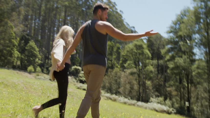 A couple walks hand in hand through a field