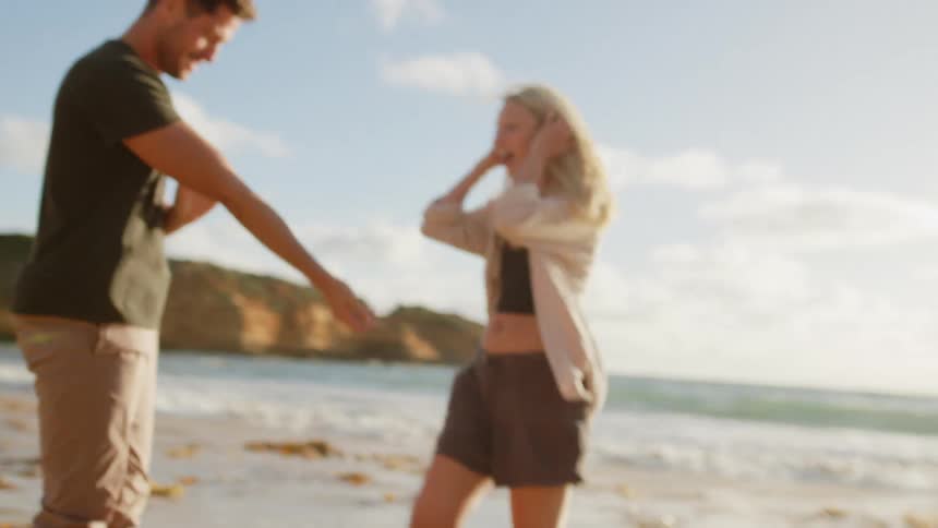 A man and woman smile while hugging each other on a beach on a summer day